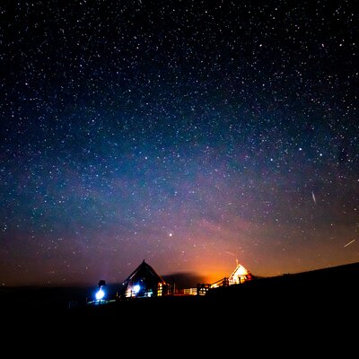 Illuminated cabins nestled amidst a starry night sky, mountains silhouetted against the warm glow of lights. | © Urlaub am Bauernhof Kärnten/ Daniel Gollner 
