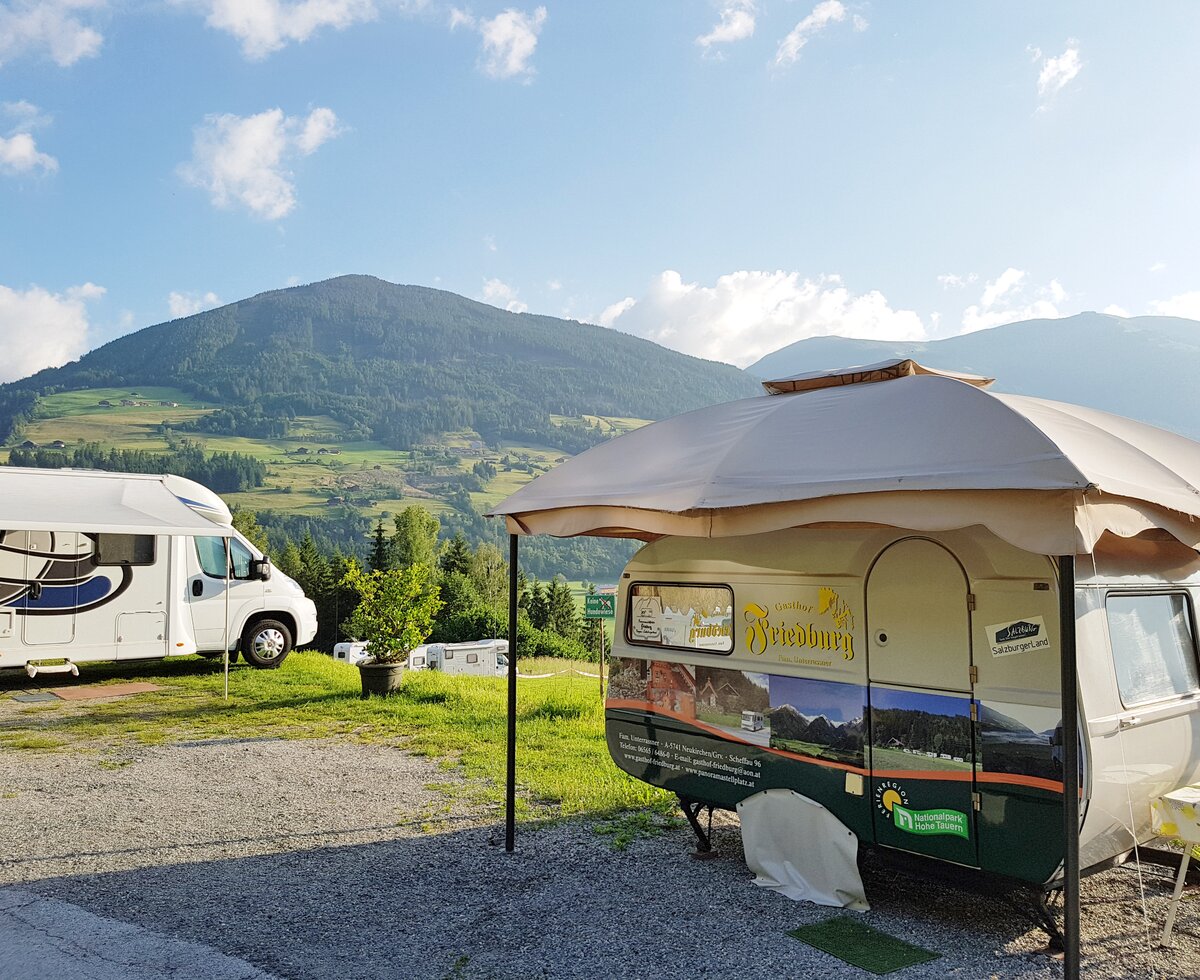 Camper van parked in a scenic mountainous landscape, with a domed tent-like structure and other camping equipment visible.